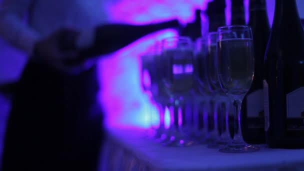 The waiter pours champagne into glasses at the celebration. Color lights party. — Stock Video