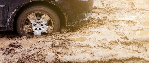 The car got stuck on a dirt road in the mud. Wheel of a car stuck in the mud on the road.