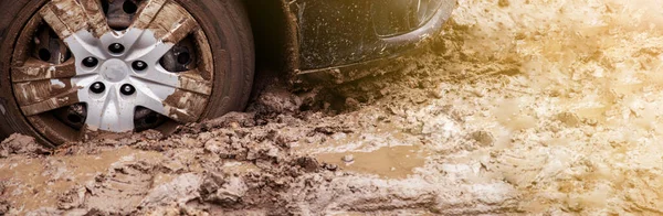 The car got stuck on a dirt road in the mud. Wheel of a car stuck in the mud on the road.