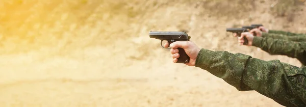 A military man in uniform, a man s hand with a gun aiming for firing a firearm.