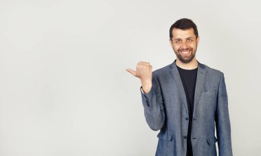 Sakallı genç adam, yan tarafa bakıyor ve reklam için bir yere başparmağıyla işaret ediyor.