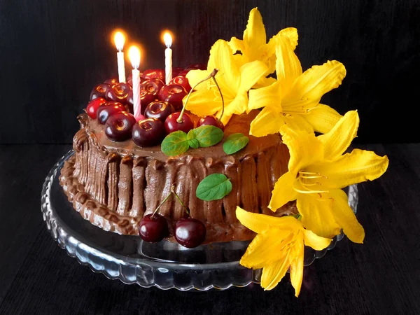 Chocolate cake decorated with cherries, candles and flowers