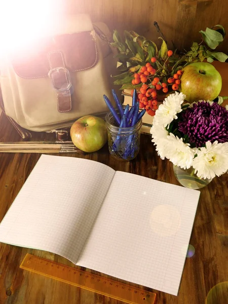 Open paper notebook with school supplies and apples in the background