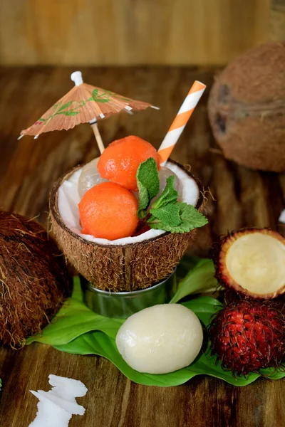 Tropical fruits: longan, rambutan and papaya ball-shaped pieces are lying in coconut. Cocktail ingredients