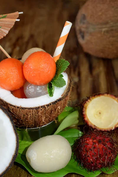 Tropical fruits: longan, rambutan and papaya ball-shaped pieces are lying in coconut. Cocktail ingredients