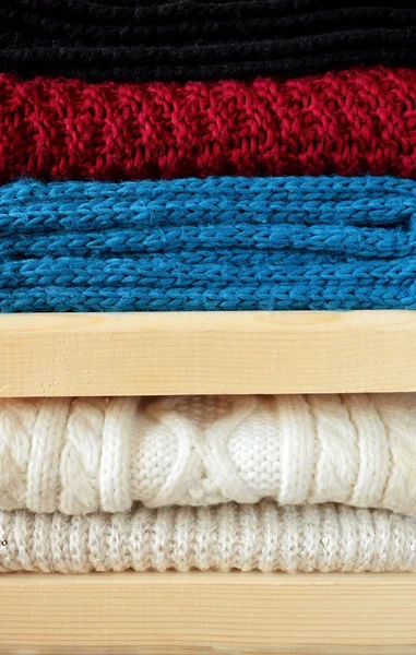 Knitted clothes are piled carefully on wooden shelves