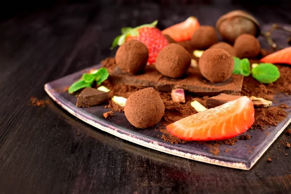 Chocolate truffles covered with cacao powder surrounded by strawberries and mint