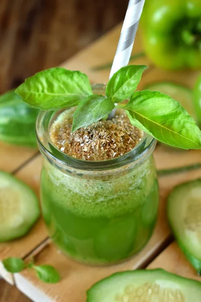 Green cocktail in a glass jar sprinkled with brans decorated with basil on wooden background