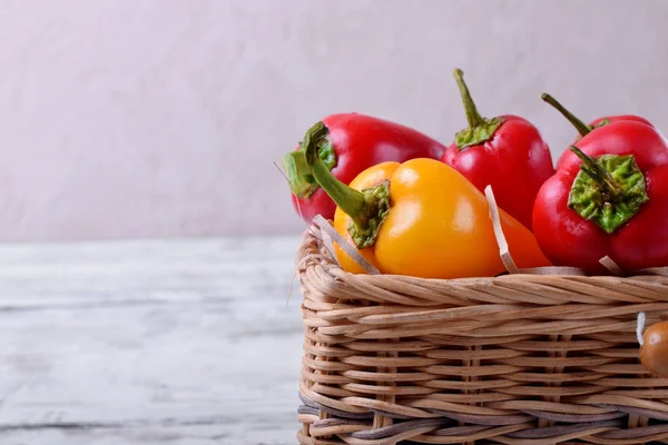 Little red and yellow bell peppers in a wicker basket against white wooden background