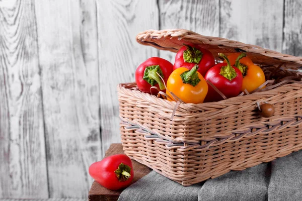 Little red and yellow bell peppers in a wicker basket against white wooden background