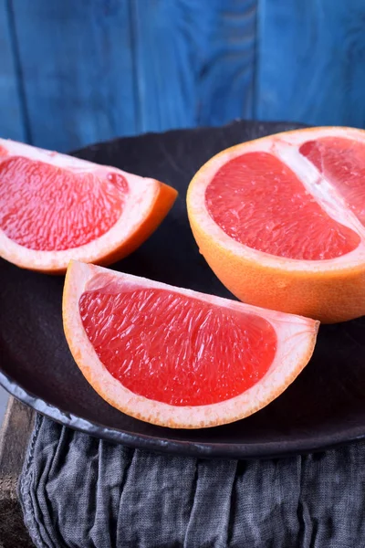 Slices of red grapefruit on the black plate against the blue wooden background