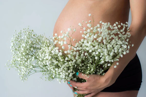 De buik van zwangere vrouw met boeket bloemen in handen — Stockfoto