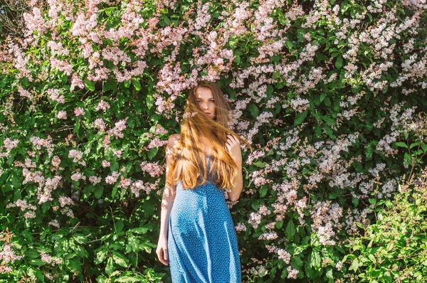 Porträtt av flicka med blont hår och blå klänning bland syren — Stockfoto