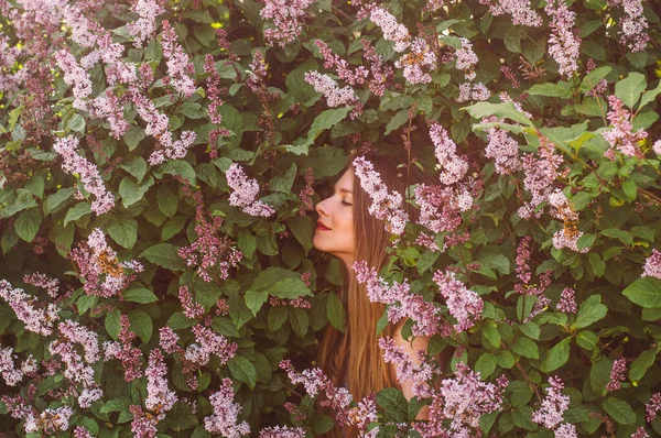 Portret van een meisje met blond haar dat bloemen ruikt onder lila — Stockfoto