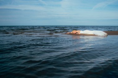 Genç sarışın gelinin portresi suyun ortasında kumlara uzanıyor.