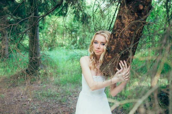 Retrato de jovem noiva loira na floresta segurando tronco de árvore — Fotografia de Stock