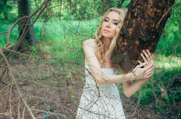 Portrét mladé blond nevěsty v lese držící kmen stromu — Stock fotografie