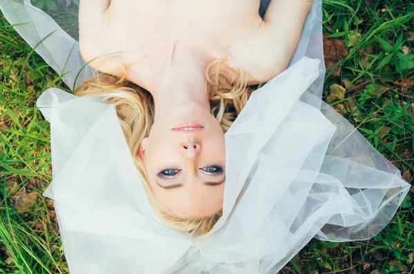 Portret van jonge blonde bruid met sluier die op gras ligt — Stockfoto
