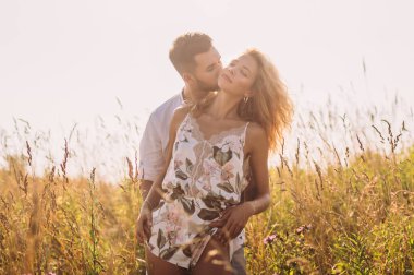 Genç adam tarlada kız arkadaşına sarılıp öpüyor.