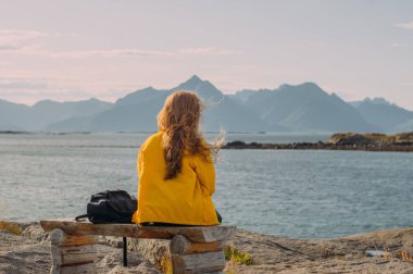 Sarı ceketli kız bankta oturuyor ve ata binmek istiyor.