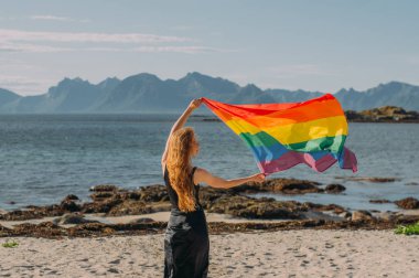 Lgbtqi bayrağı taşıyan genç sarışın kız gündüz yürüyor.