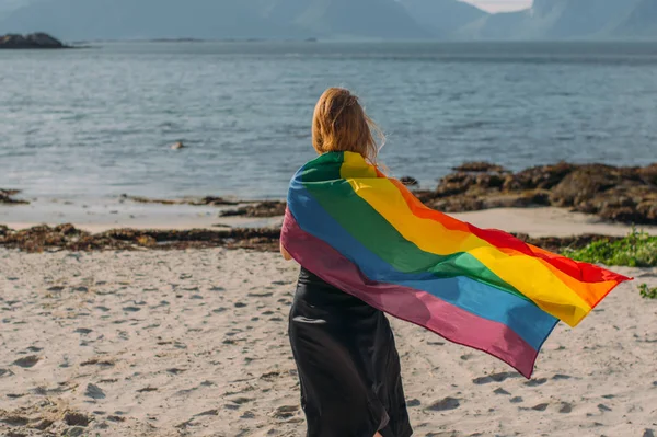Chica rubia joven cubierta con bandera LGBTQI caminando en el día a día — Foto de Stock