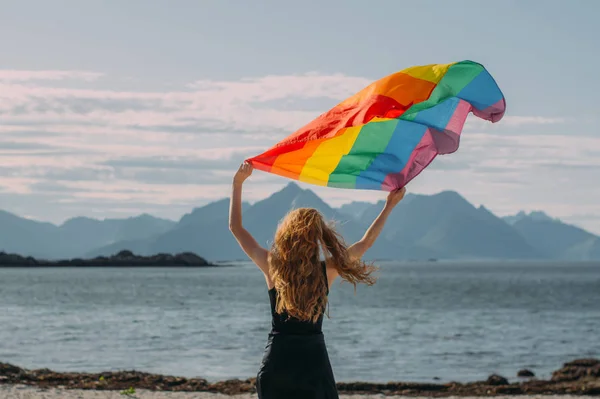 Joven chica rubia sosteniendo bandera LGBTQI por encima de la cabeza caminando en el — Foto de Stock