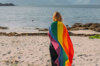 Lgbtqi bayrağıyla kaplanmış genç sarışın kız gün içinde yürüyor.