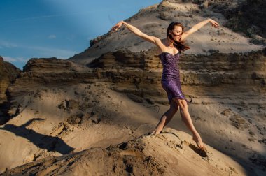 Kum yamacında dans eden mor parlak elbiseli kahverengi saçlı kadın.