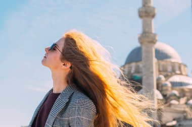 Sarışın ve kapalı gözlü güzel kız, eski İstanbul kentinde Süleyman Camii ve İstanbul Boğazı manzaralı duruyor