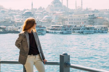Sarışın güzel kız, İstanbul seti üzerinde Süleyman Camii ve İstanbul Boğazı manzaralı duruyor.