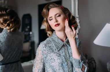 Kaliteli makyajlı, saç stili ve eli yüzüne yakın güzel sarışın kız aynanın yanında kapalı gözlerle duruyor.