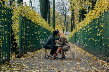 Sandalyelerin ve öpücüklerin ortasında bir çift, bir sürü sarı ağaçla sonbahar mevsimi.