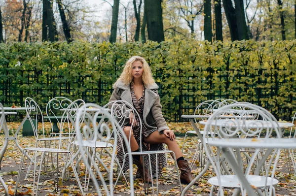 Genç Sarışın Kız Sonbaharda Parktaki Masada Oturuyor Kameraya Bakıyor — Stok fotoğraf