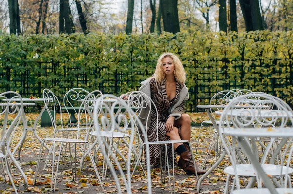 Genç Sarışın Kız Sonbaharda Parktaki Masada Oturuyor Kameraya Bakıyor — Stok fotoğraf