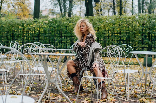 秋天的时候 金发姑娘坐在公园的桌子旁 看着镜头 — 图库照片