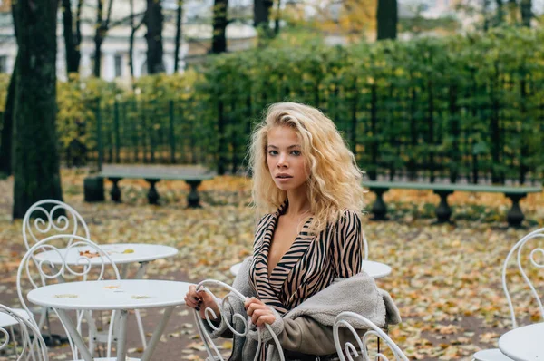 秋天的时候 金发姑娘坐在公园的桌子旁 看着镜头 — 图库照片