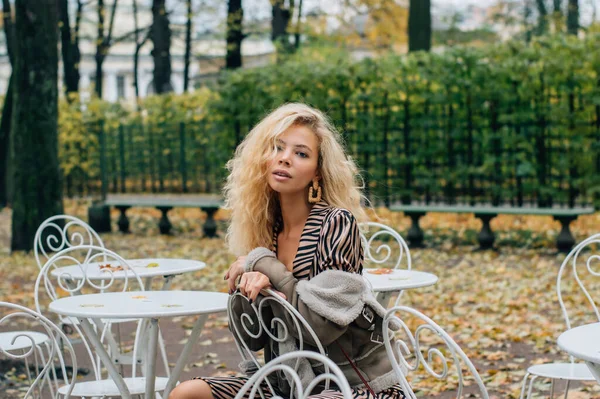 Молода Блондинка Усміхнена Дівчина Сидить Столом Громадському Парку Восени Дивиться — стокове фото