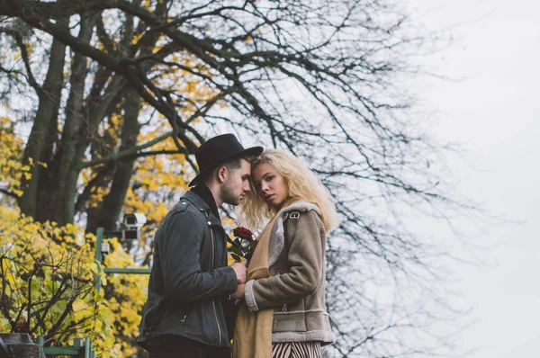 Halk parkında yürüyen ve kucaklaşan çiftler, bir sürü sarı ağaçla sonbahar mevsimi.