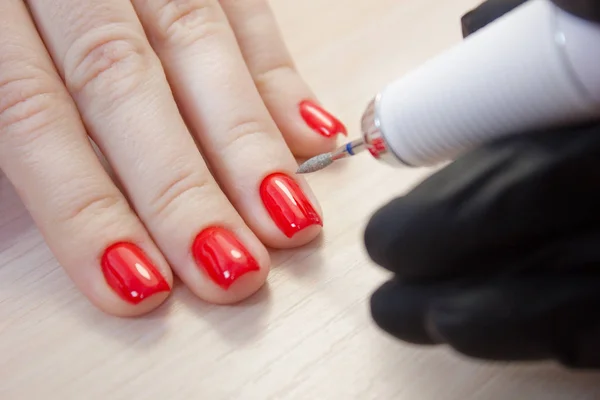 El maestro utiliza una máquina eléctrica para quitar el esmalte de uñas en las manos del cliente durante la manicura de hardware en el salón. Concepto de belleza y cuidado de uñas — Foto de Stock