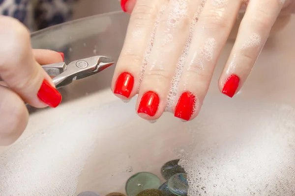 Una mujer hace una manicura con una herramienta. Clavos rojos empapados en un baño con agua — Foto de Stock