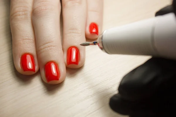 El maestro utiliza una máquina eléctrica para quitar el esmalte de uñas en las manos del cliente durante la manicura de hardware en el salón. Concepto de belleza y cuidado de uñas — Foto de Stock