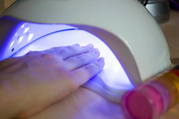 Professional ultraviolet nail manicure lamp drying shell gel polishing on womans hand in a beauty salon