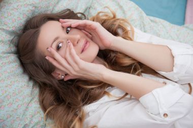 Kadın yatakta yatarken ve yüz elleriyle dokunuyor