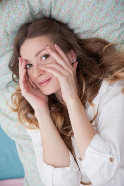 Kadın yatakta yatarken ve yüz elleriyle dokunuyor