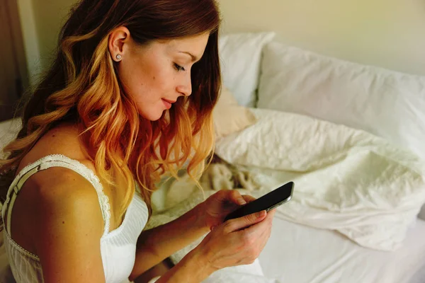 Mujer sentada en la cama y mirando el smartphone — Foto de Stock