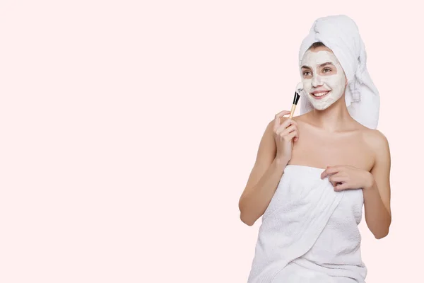ブラシで白い保湿マスク彼女の顔に彼女の頭の上の白いタオルでの美しい少女 粘土マスク 化粧品 治療泥 — ストック写真