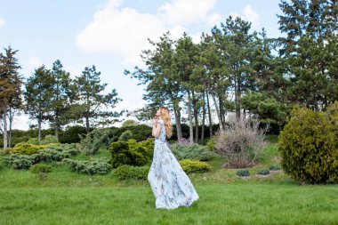 Yaz park, yeşil bitkiler, ağaçlar ve zemin üzerine mavi bulutlu gökyüzü uyanma mavi elbiseli güzel kadın     