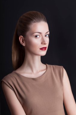 Portre studio şık makyaj ve saç ile genç kadın bir at kuyruğu toplanan bej elbise, siyah arka plan üzerinde duran Güzellik Portresi