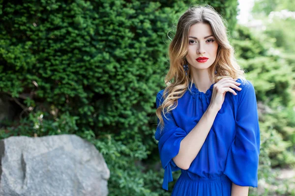 立って 青いドレスを着てスタイリッシュなメイクと美容の若い女性の肖像画の花の庭園 緑の植物の背景 — ストック写真